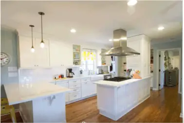 Bright white kitchen with an island, stainless steel range hood, pendant lights, and hardwood floors.