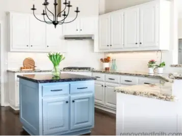 Bright kitchen with white cabinets, granite countertops, a blue island, a chandelier, and a vase of tulips.