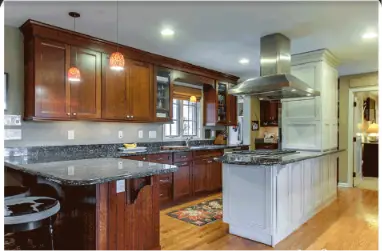 Kitchen with dark wood cabinets, granite counters, and a central island with a stainless steel range hood; pendant lights and hardwood floors are visible.