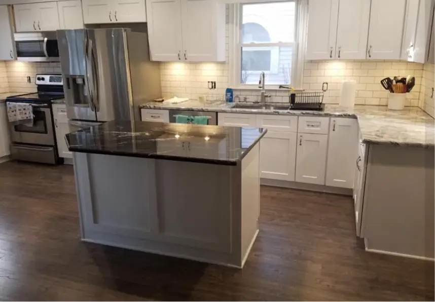Bright white kitchen with an island, dark granite countertop, and stainless steel refrigerator, stove, and sink under a window.